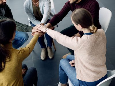 Close-up of people supporting each other and gather hands in unity during group therapy.