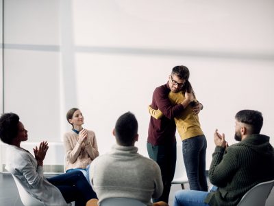 Participants of group therapy applauding while young couple is embracing after a session. Copy space.