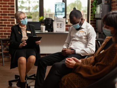 Woman therapist talking to african american man at support group therapy, sitting in circle. People at aa meeting discussing alcohol addiction and mental health problems, wearing face masks.